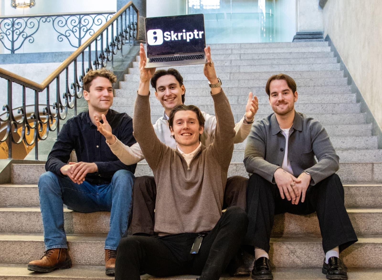The four Skriptr founders holding up a laptop showing the Skriptr logo.